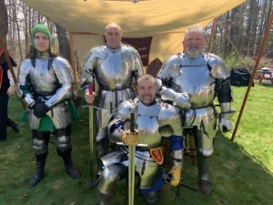 The Knights of Lord Talbot pose for a photo for the Gardiner News. Photo depicts 4 people in 15th century plate armor posing under a sun shade.